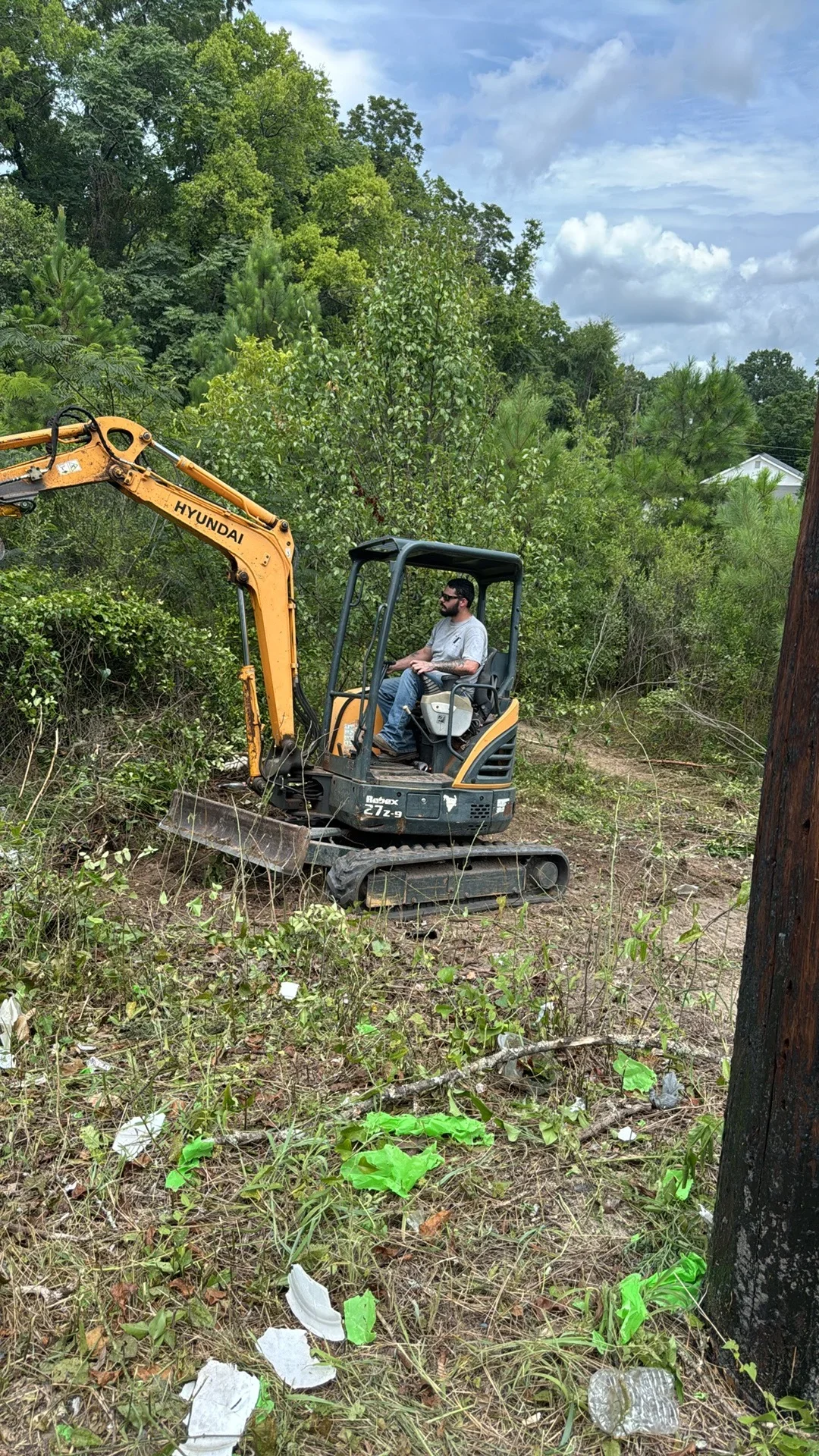 Compact excavator clearing overgrown vegetation and brush from residential lot