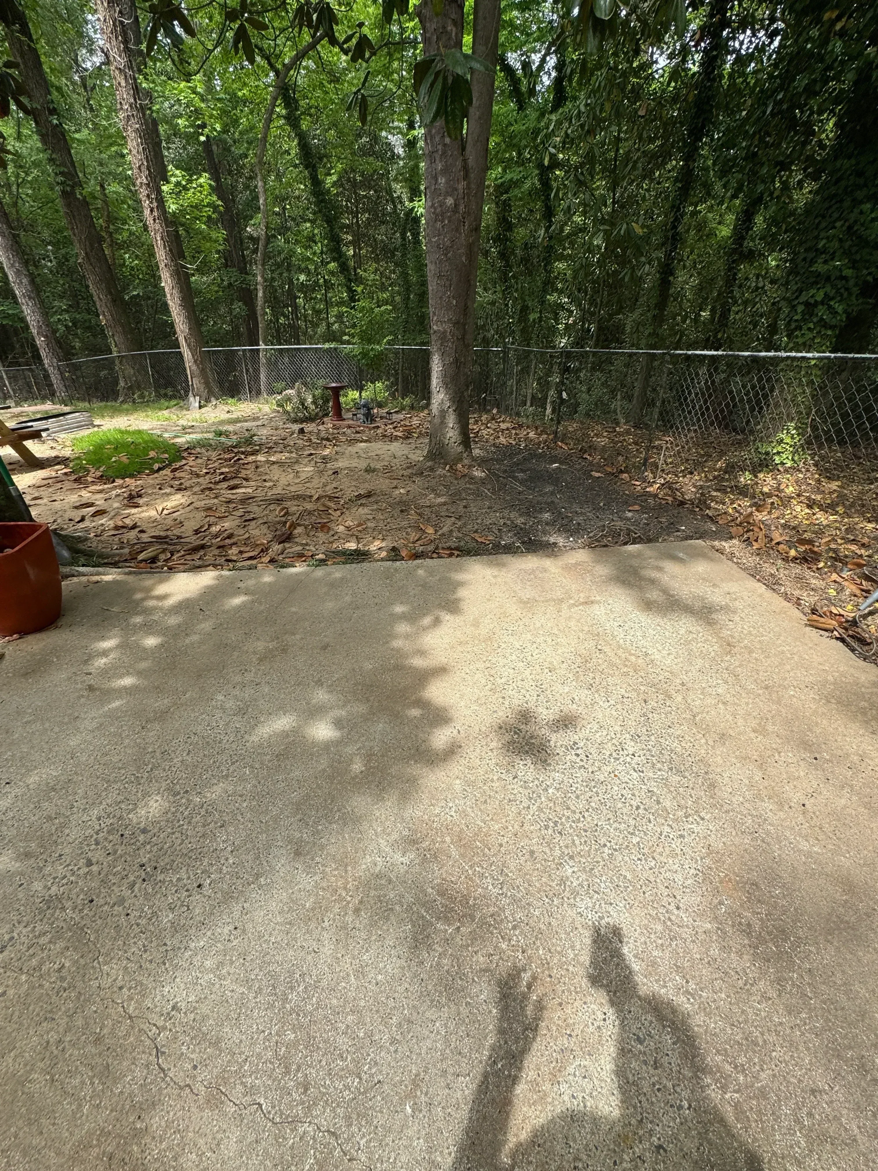 Demolished concrete driveway with exposed base, metal fence, and green vegetation visible
