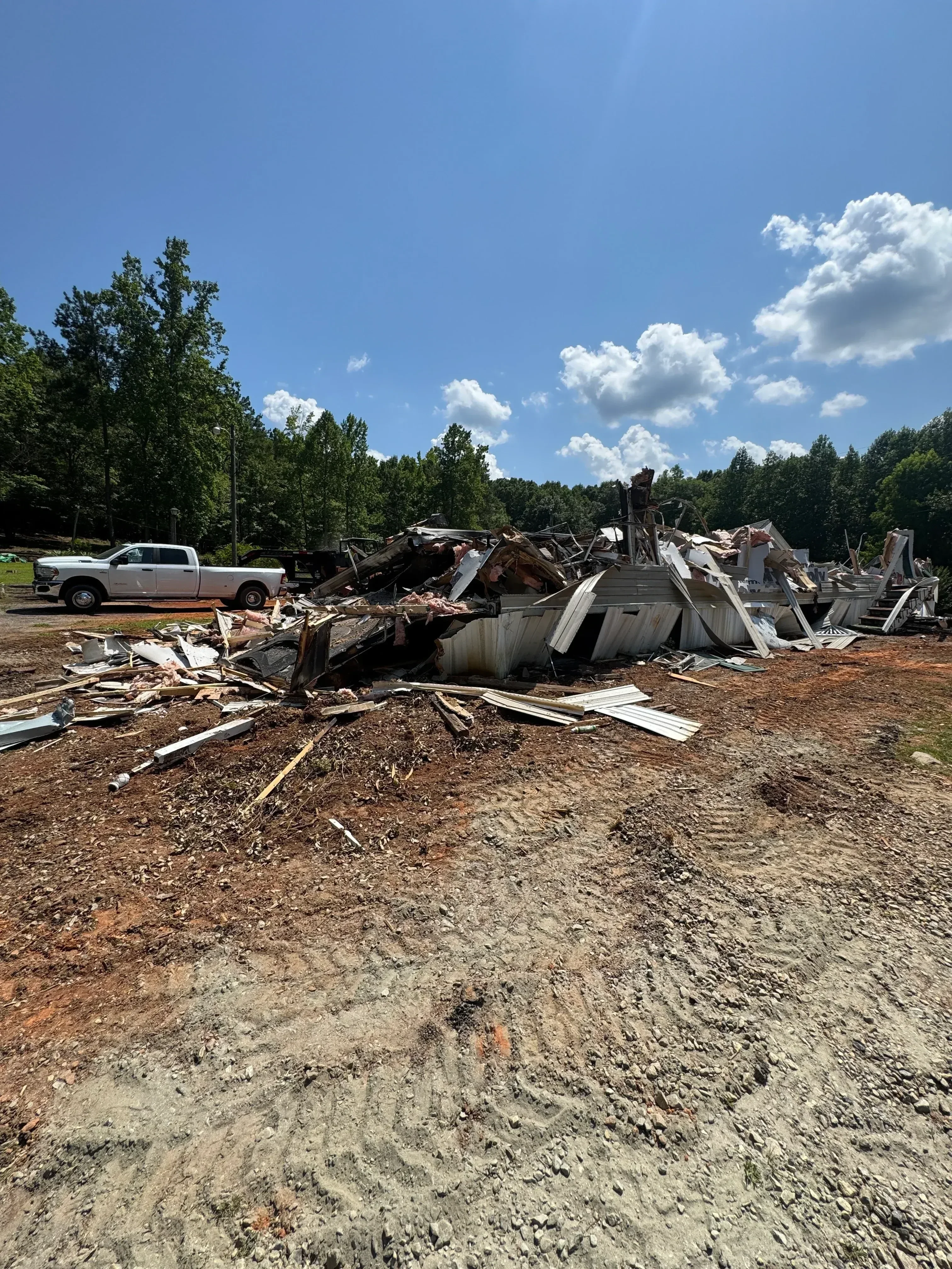 Demolished residential structure with sorted debris and white hauling trucks on-site
