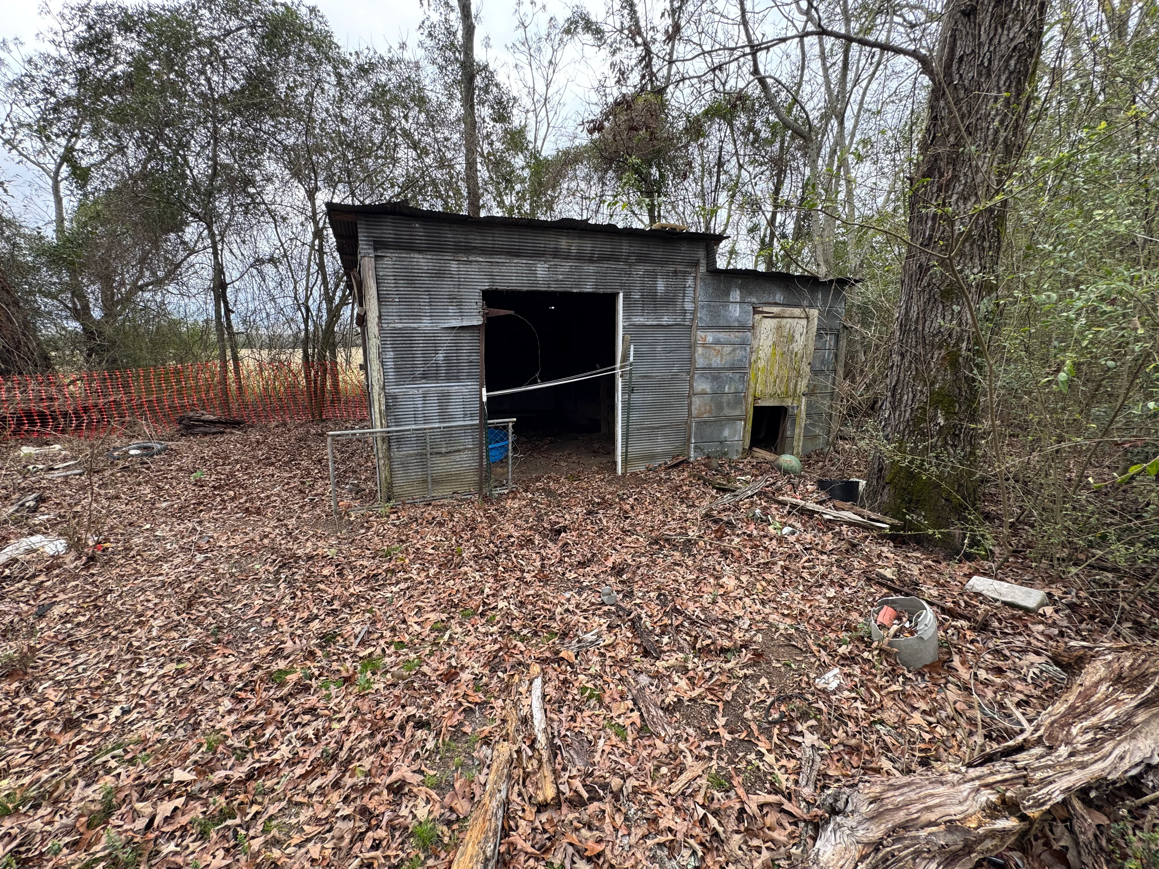 Corrugated metal residential structure demolition with safety fencing in wooded area