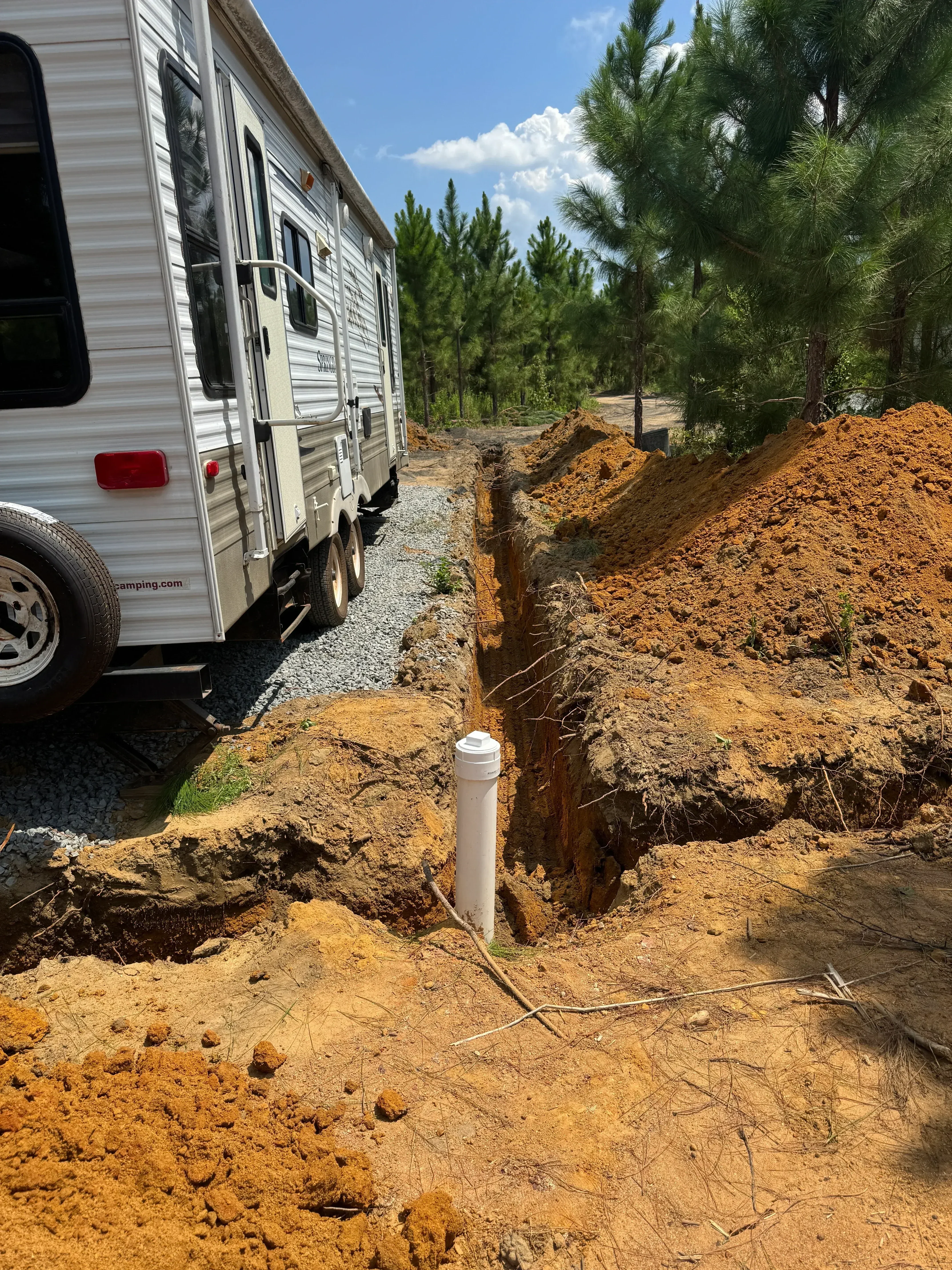 Excavated trench with PVC pipe installation and graded soil layers at residential site