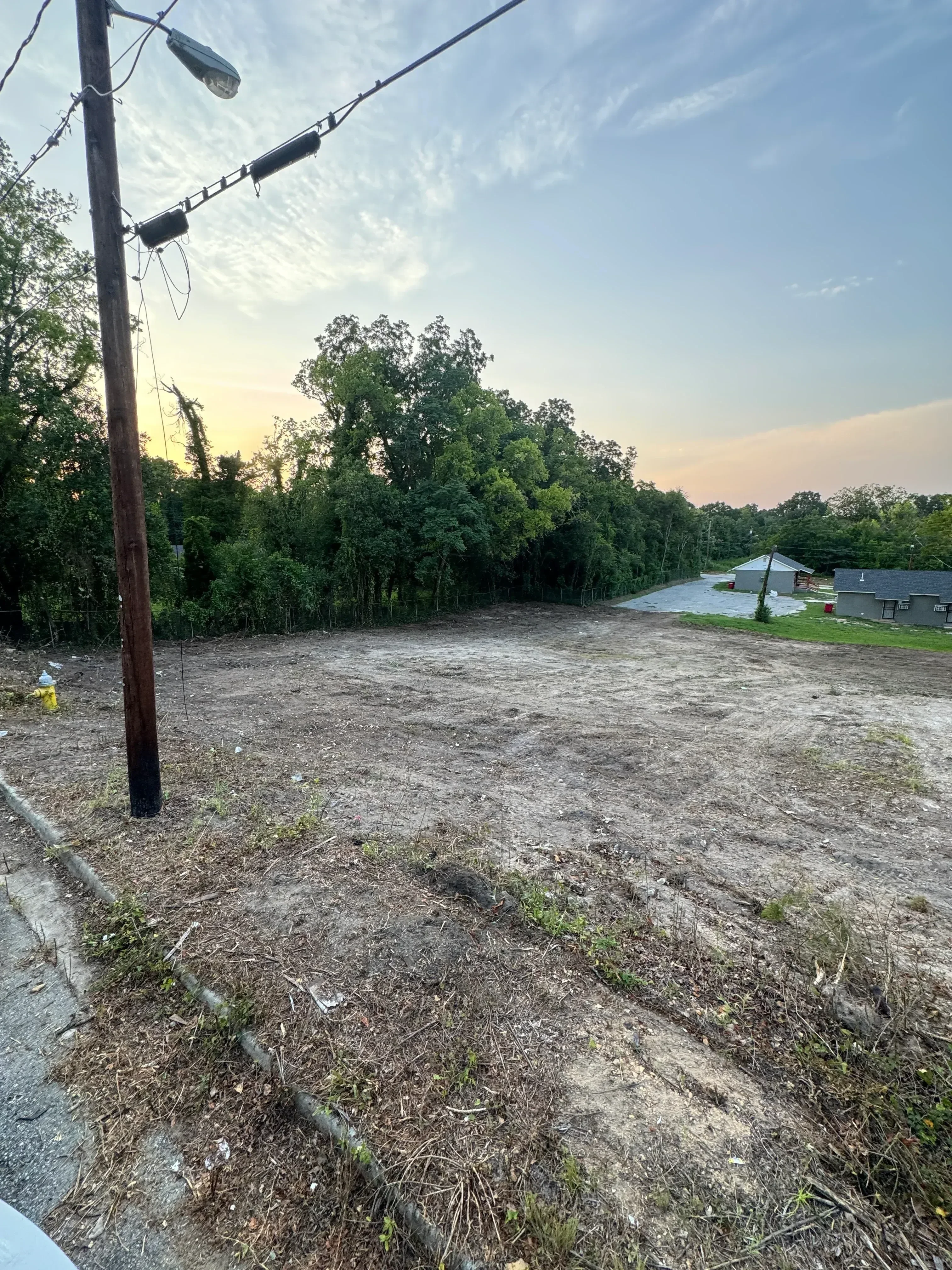 Cleared residential lot with bare earth, gravel base, and preserved trees along property edge