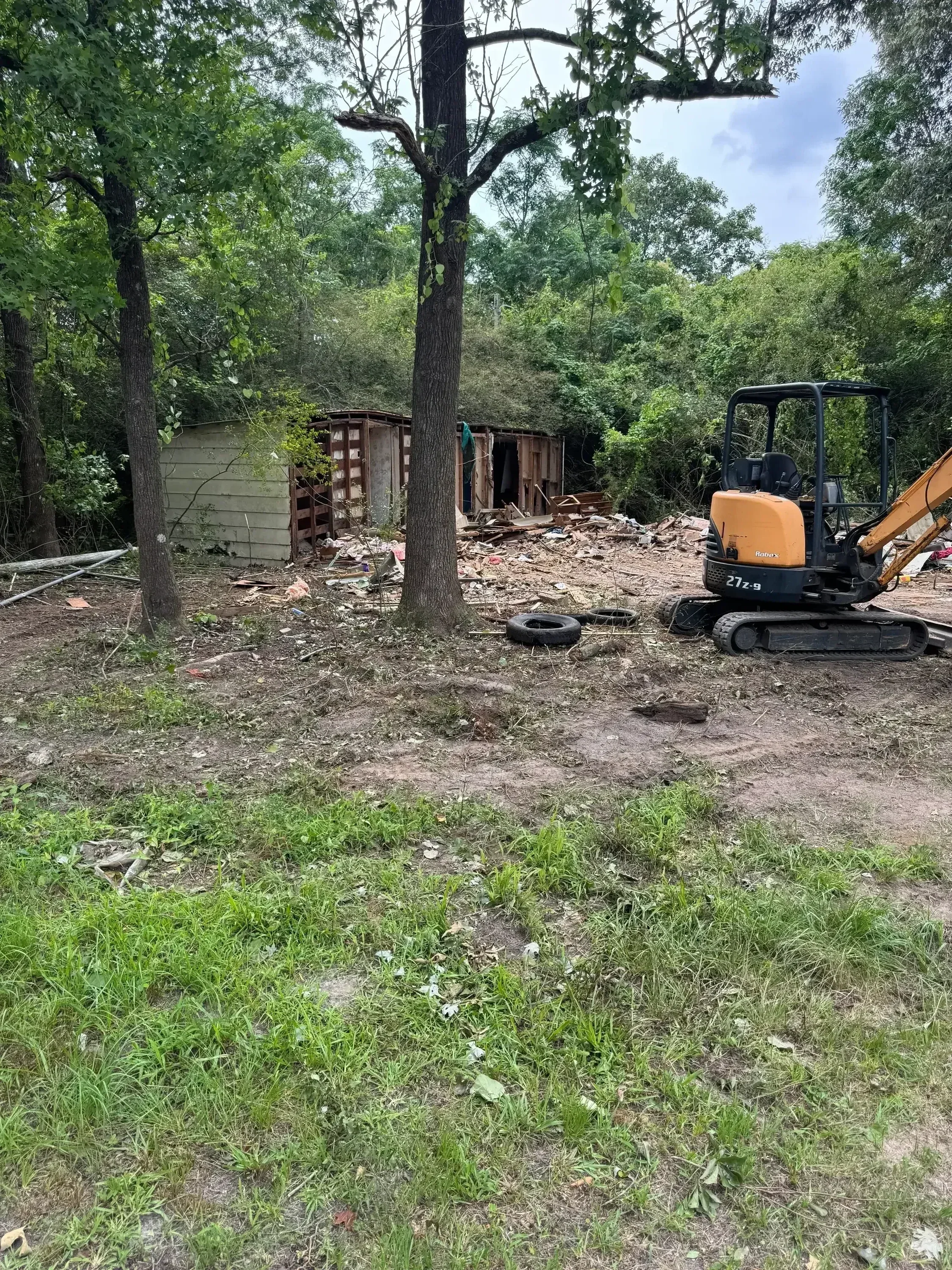 Excavator with grapple bucket demolishing wooden residential structure and collecting debris