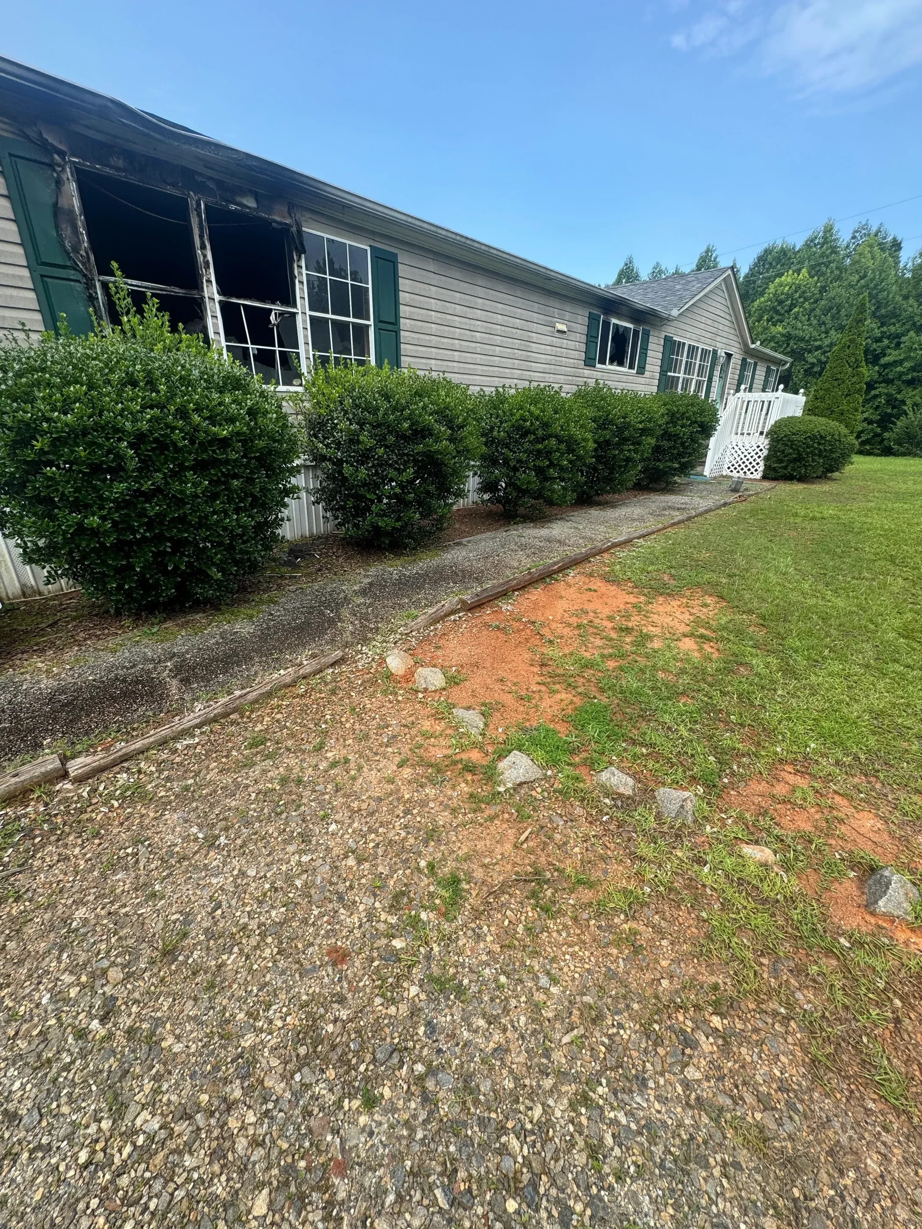 Cleared residential driveway with gravel base, metal-sided building, and manicured landscaping